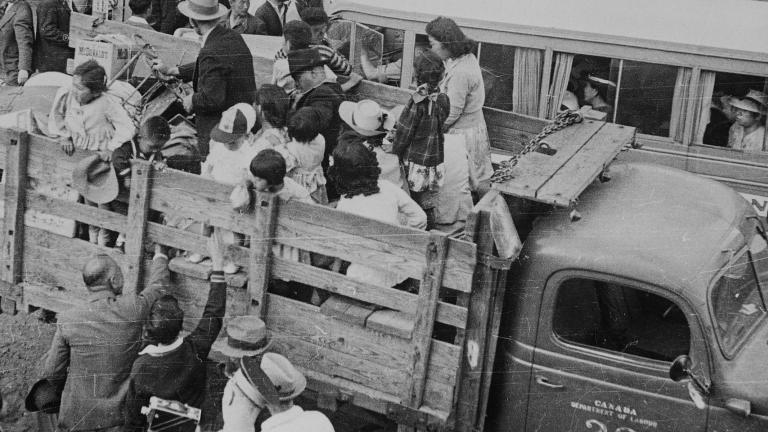 A black-and-white photograph of people being loaded onto trucks as others behind them wait in line.