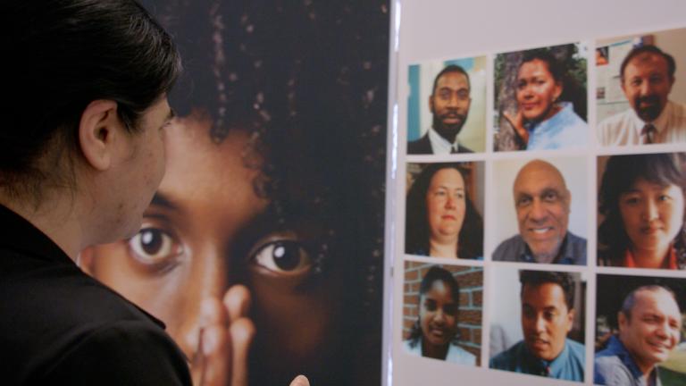 A woman gazes at a display showing faces of a diverse group of people. Partially obscured.