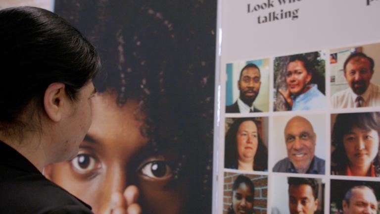 A woman gazes at a display showing faces of a diverse group of people. Partially obscured.