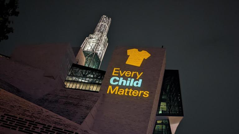 An image of an orange shirt with the text Every Child Matters is projected on an exterior wall of the Museum. Partially obscured.