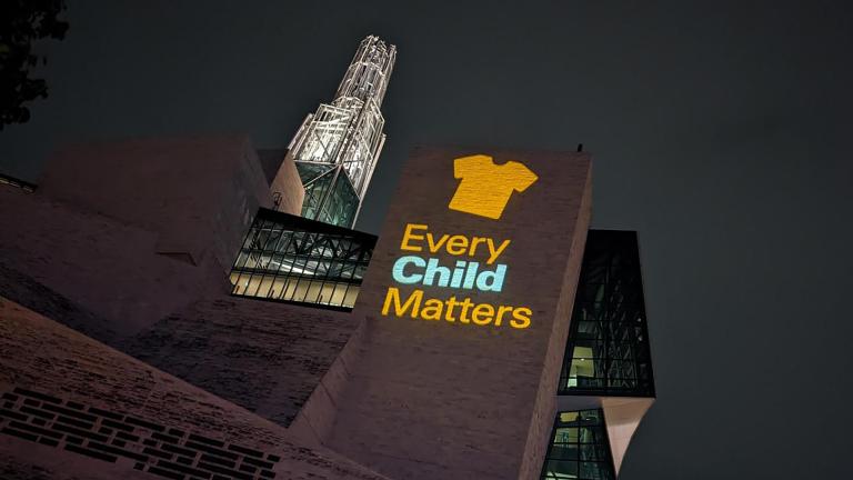 An image of an orange shirt with the text Every Child Matters is projected on an exterior wall of the Museum. Partially obscured.