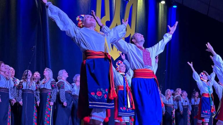 An ensemble of Ukrainian performers dancing on stage; those in the front are looking and reaching up with their arms.