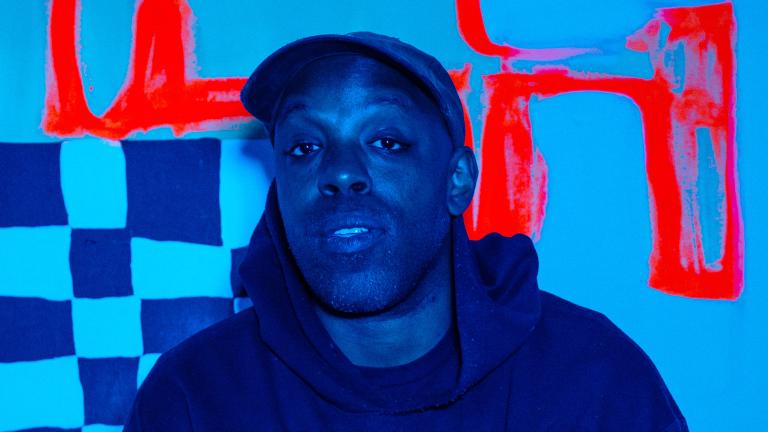A blue-toned image of a black man wearing a cap and dark hoodie in front of a checkered backdrop with thick red lines. Partially obscured.