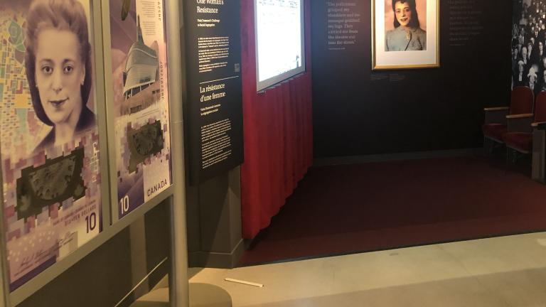A museum exhibit that resembles an old-fashioned movie theatre. On one side are large representations of a $10 Canadian banknote featuring a woman’s face. Partially obscured.