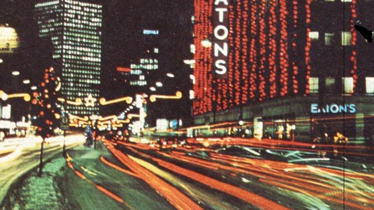 Late 1960s-era photo of downtown Winnipeg showing the Eaton’s building decorated with many bright Christmas lights. Partially obscured.