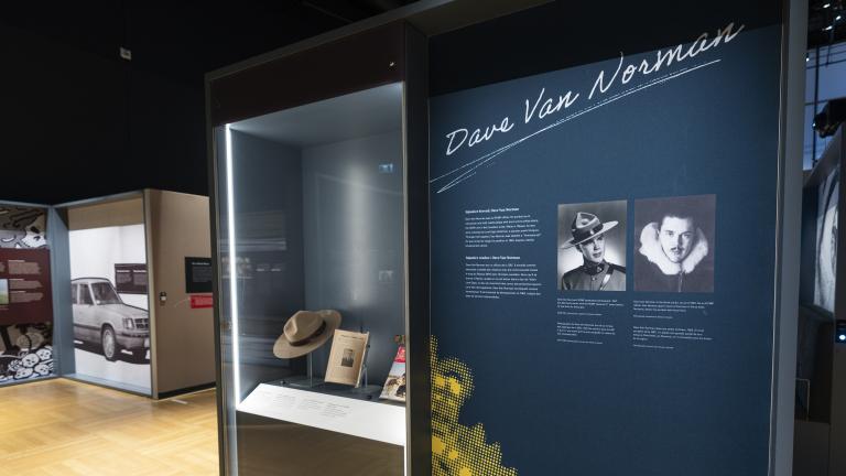 A display case featuring a Stetson hat and magazines is to the left of an exhibition panel with photographs, text, and the words “Dave Van Norman.”