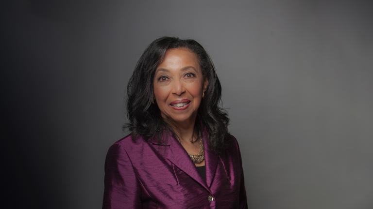 A portrait of a Black woman with long hair wearing a plum-coloured jacket. Partially obscured.