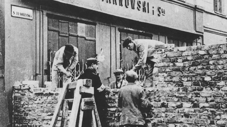 A group of men building a stone wall across a city street Partially obscured.