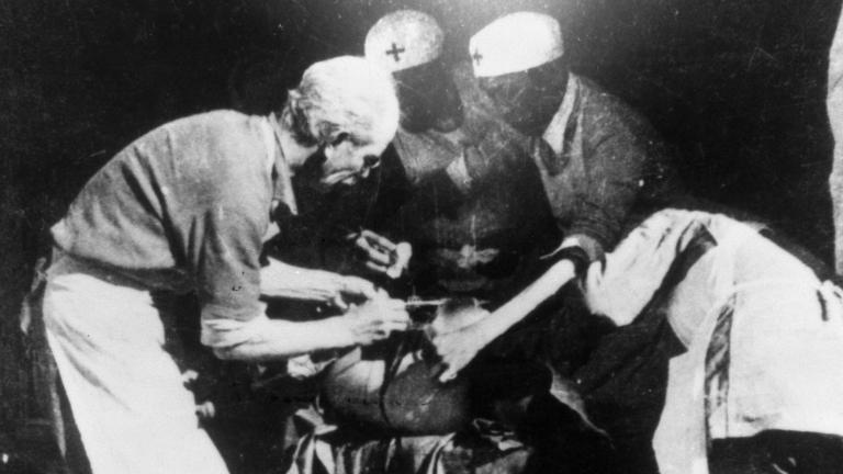 Four people standing around an operating table. Partially obscured.