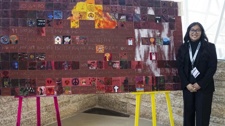 Students standing next to their large artwork displayed on easels. Partially obscured.