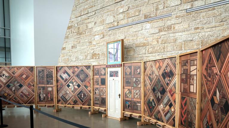 Right view of a structure of vertical wood panels covered in patterns of images, with a white wooden door at the centre.