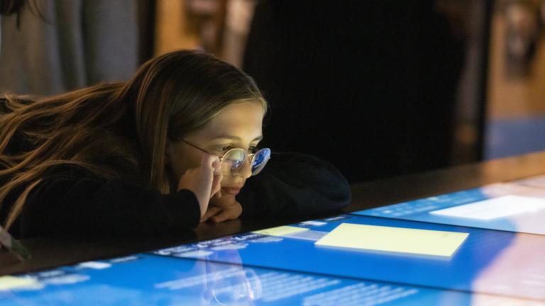 A girl looks at a horizontal interactive display with interest. Partially obscured.