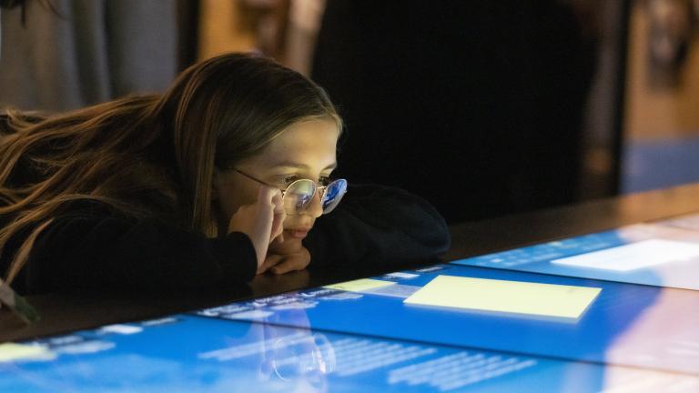 A girl looks at a horizontal interactive display with interest. Partially obscured.
