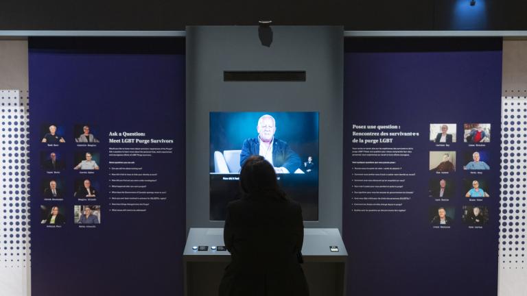 A person with their back to us watches a video. Small portraits of people flank the video monitor on the left and right.
