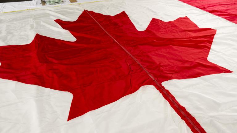 A close-up image of a Canadian flag, with a focus on the red maple leaf. Partially obscured.