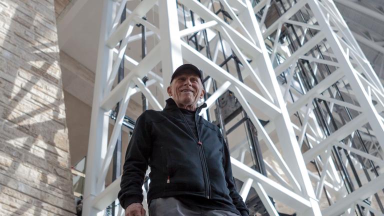 Antoine Predock, the architect of the Museum, is pictured inside the Museum from a low angle with white beams rising above him.