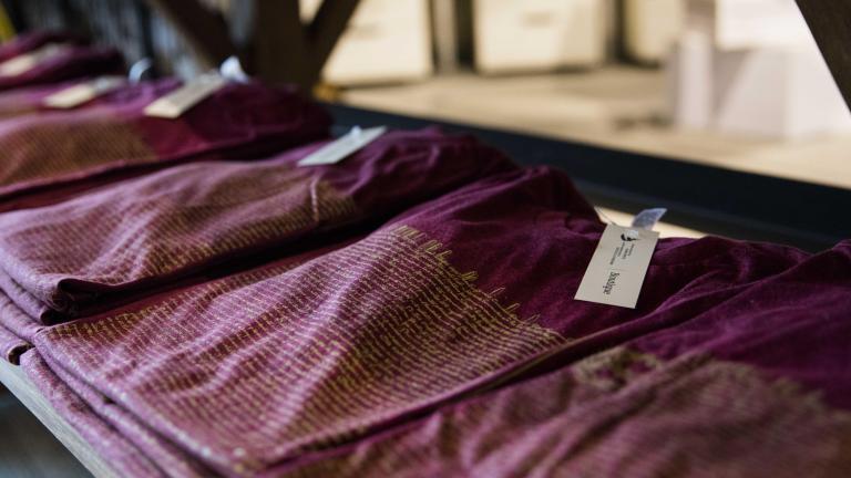 Stacks of three or four folded burgundy t-shirts lay on a wooden table. Partially obscured.