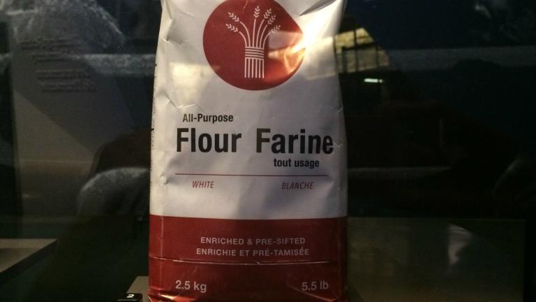 A bag of flour on display. The text reads: All-Purpose Flour/Farine tout usage, White/Blanche, Enriched & Pre-Sifted/Enrichie et pré-tamisée, 2.5 kg/5.5lb