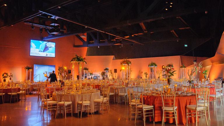 A large room with high ceilings, filled with round tables that have formal table settings. 