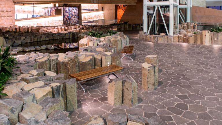 Stone pillars ranging from about one to two feet high are grouped together and jutting out of the floor. Two wooden benches sit in the centre of the image.
