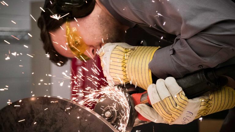 Close-up of a person in coveralls sending sparks flying while grinding metal.