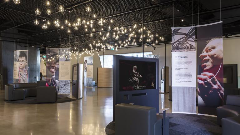 A museum display consisting of curved couches, video screens, and larger-than-life photos of diverse people.