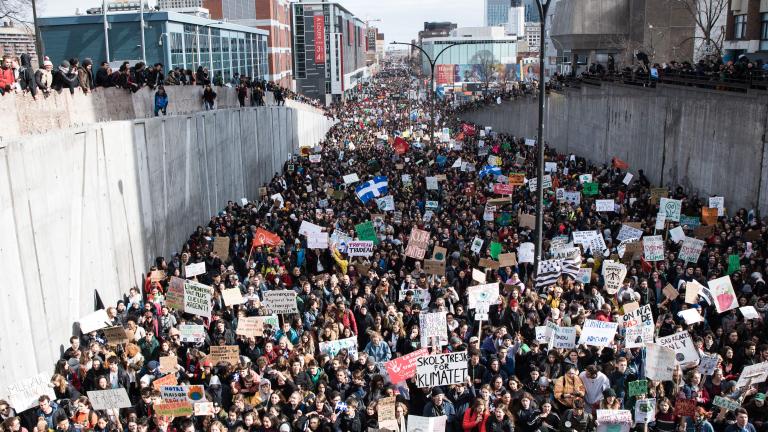 Thousands of people are holding protest signs and banners while marching in a street.