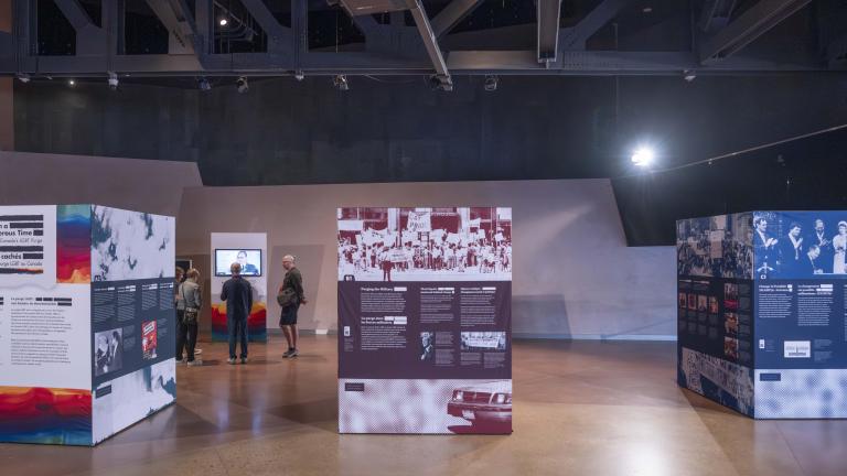 Three large cubes, taller than a person and arranged side-by-side, are covered with images and text. These cubes are the pop-up exhibit Love in a Dangerous Time.