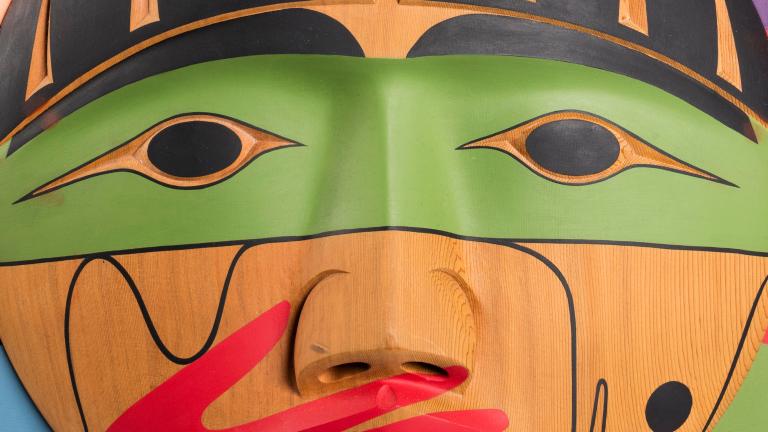 A carved wooden box, showing the carved face of a person with a painted red hand over their mouth. Partially obscured.