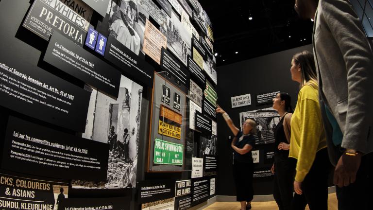 Four people of different ages and ethnicities reading museum displays. Partially obscured.
