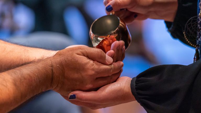 A person pours water from a copper cup into the cupped hands of another person. Partially obscured.