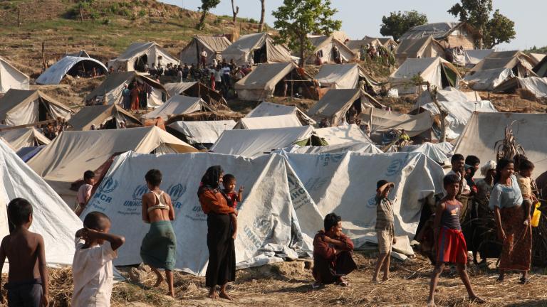 A densely packed camp of canvas tents on a hillside. Many people are visible inside and outside the tents.