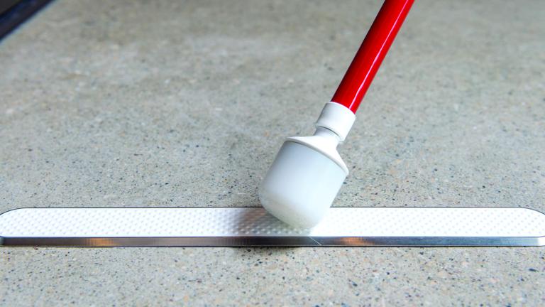 The end of a cane touches a raised strip attached to the floor.