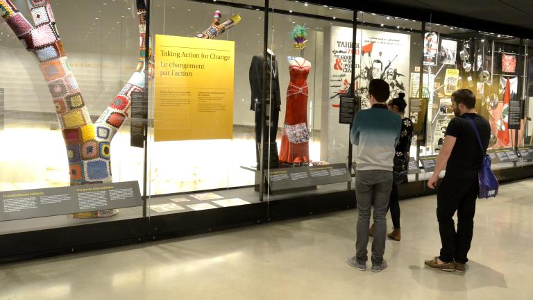 Museum visitors observe a glass display containing images and objects.