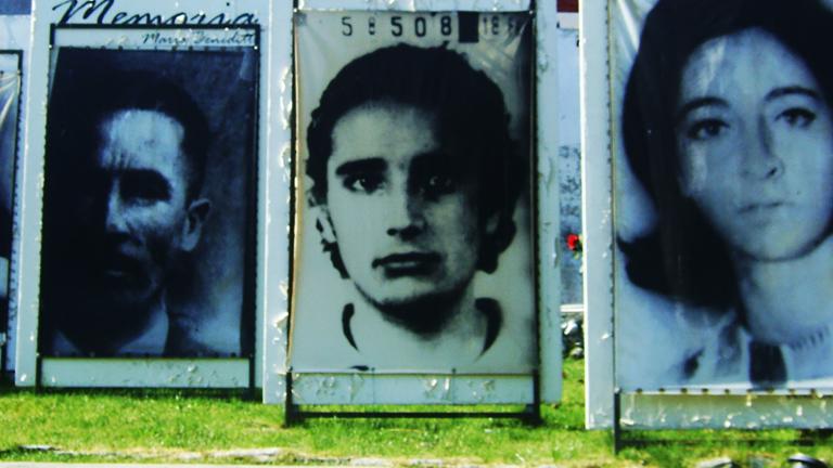 Outdoor display of large photographs of people’s faces. Partially obscured.
