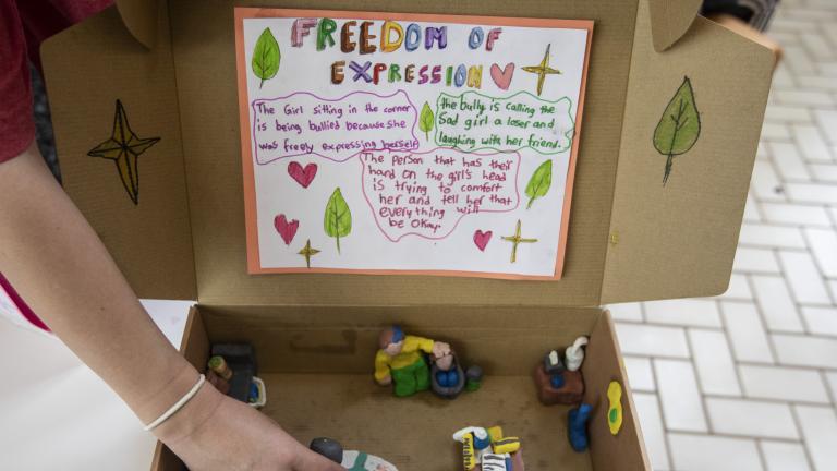 An open cardboard box with a scene of people interacting made of clay. 