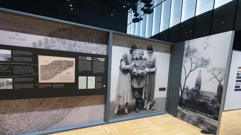 A large exhibit panel with text and historical images is on the left. On the right is a large black-and-white photograph from the 1910s of a man in a military uniform flanked by two women in dresses. A photograph of a large building can be seen further to the right.