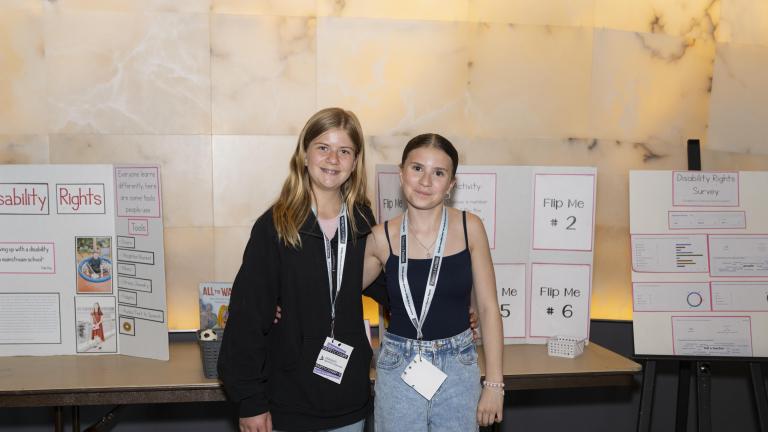 Two students standing in front of a table and an easel that are displaying presentations on poster boards. 