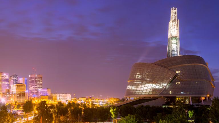 A panoramic shot of the Museum and the Winnipeg skyline at dusk. Partially obscured.