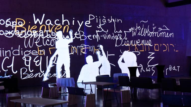Interactive screen depicts human figures writing “welcome” in several different languages. Partially obscured.