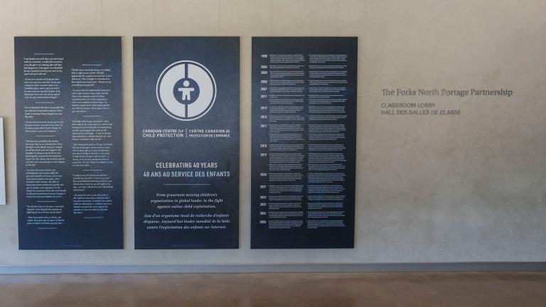 Large dark blue panels with white text and graphics displayed in the Community Corridor at the Canadian Museum for Human Rights. The centre panel features a circular logo and commemorates the 40th anniversary of the Canadian Centre for Child Protection. The two panels on either side present bilingual text in English and French. Partially obscured.