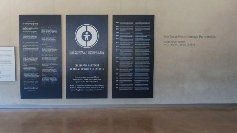 Large dark blue panels with white text and graphics displayed in the Community Corridor at the Canadian Museum for Human Rights. The centre panel features a circular logo and commemorates the 40th anniversary of the Canadian Centre for Child Protection. The two panels on either side present bilingual text in English and French. Partially obscured.