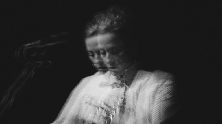 Black-and-white photo of Sarah Harmer playing guitar. It appears like two fuzzy images are juxtaposed one on another. Partially obscured.
