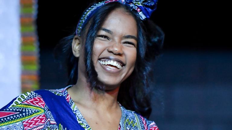 A black woman wearing traditional African dress is smiling and dancing.