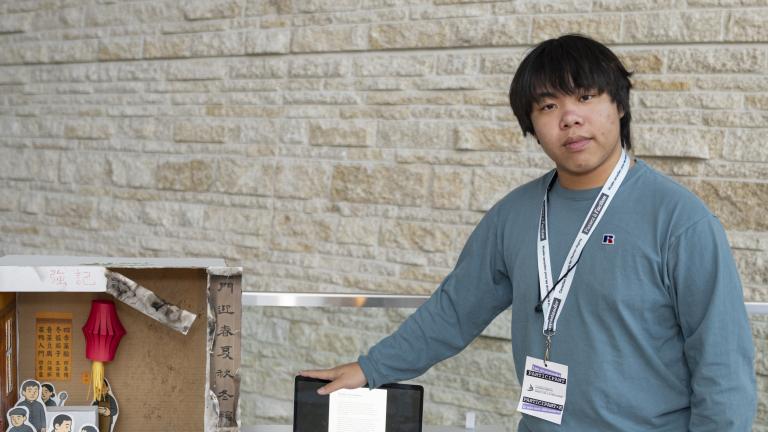 A young man stands next to a display resembling a Chinese restaurant. One side is tidy and has illustrations of people eating food. The other side is empty and damaged.