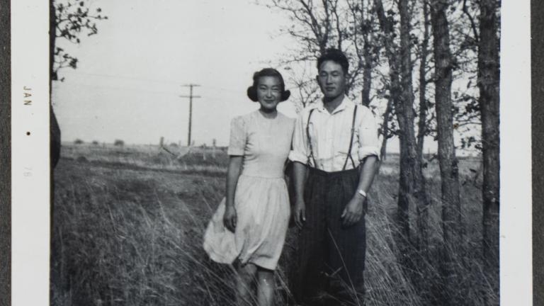 A young Japanese Canadian couple pose in a field with trees in the background. Partially obscured.