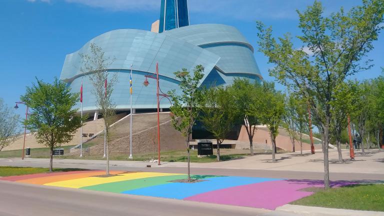 A rainbow crosswalk in front of the Canadian Museum for Human Rights on a sunny day Partially obscured.