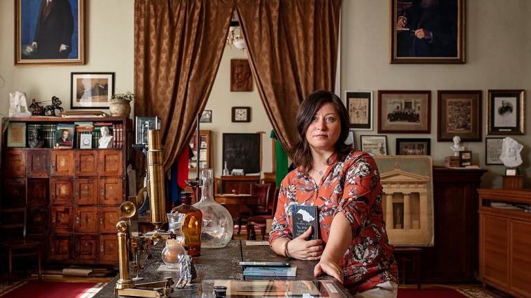 A woman kneels beside a coffee table surrounded by books and heirlooms. Partially obscured.