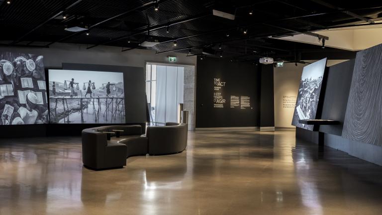 A museum gallery featuring photographs projected onto large screens with seating in the middle of the room.