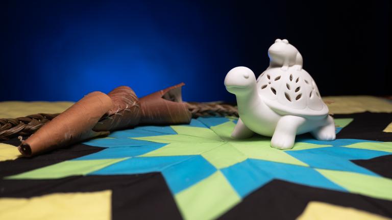 A white figure of a turtle with a frog on its back sitting on top of a colourful star blanket.